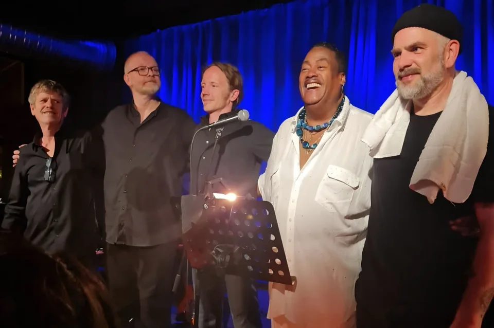 Keith mit vier Musikern vor einem blauen Bühnenvorhang
